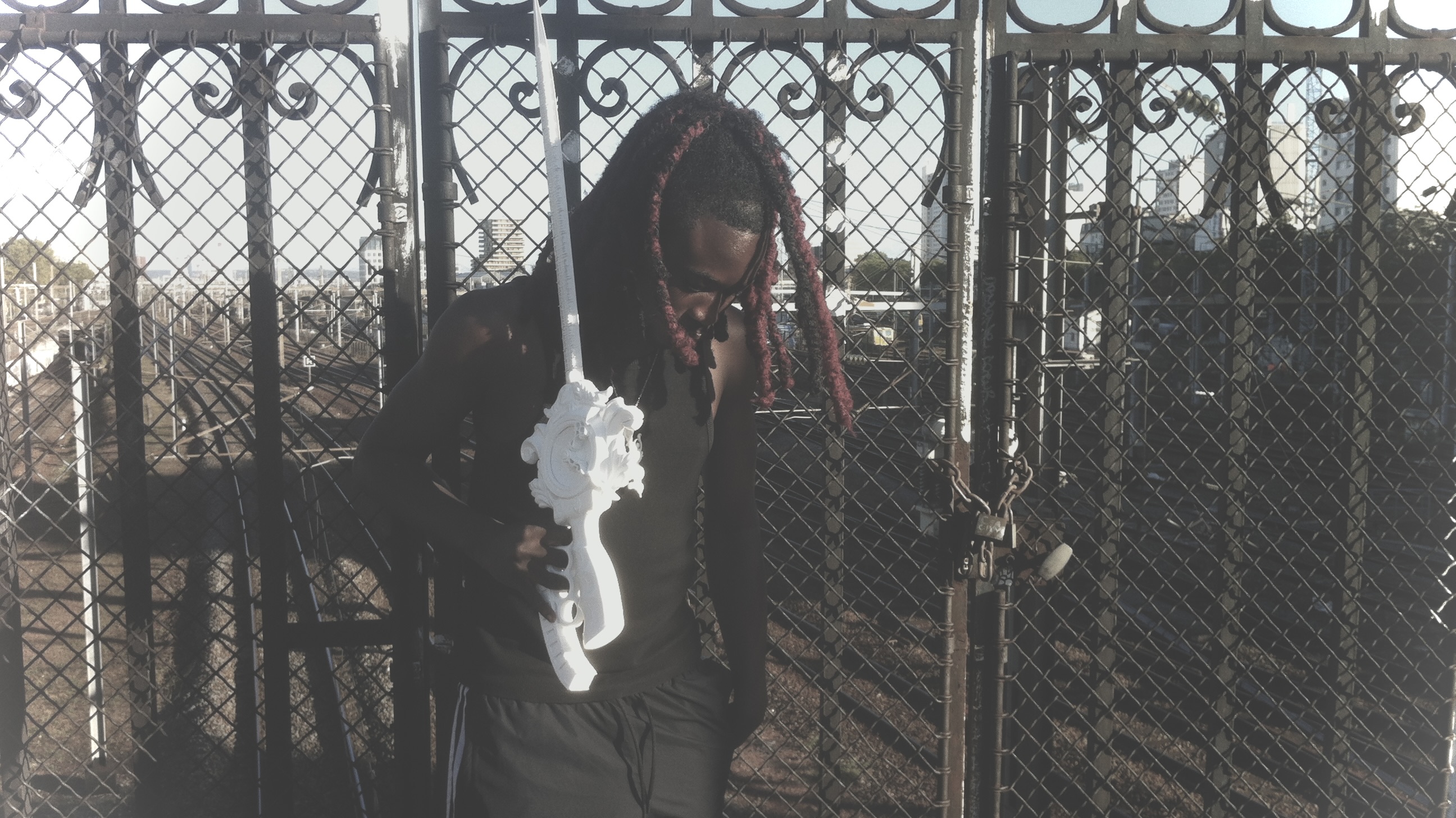 Portrait holding an ornate white printed object beside a metal fence