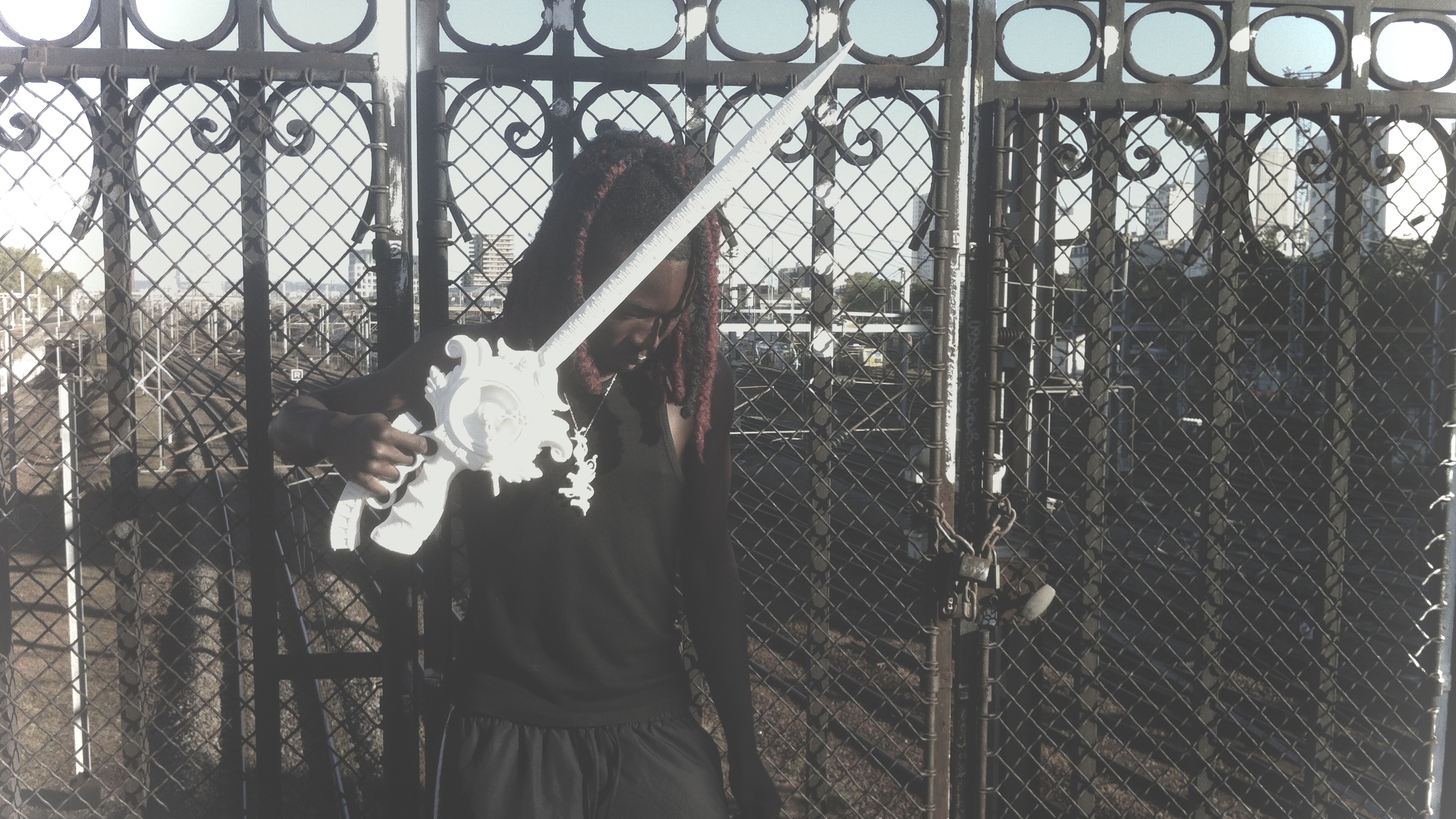 White ornate printed object held diagonally beside a metal fence